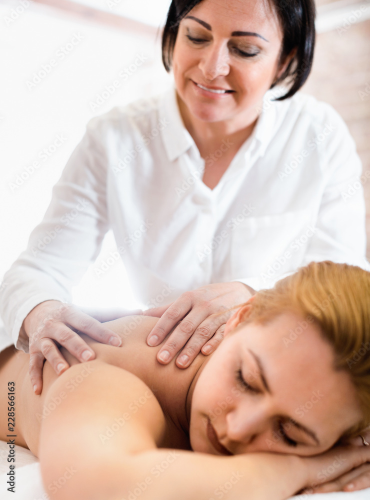 Fototapeta premium Adult masseuse makes relaxing massage shoulder zone to young woman