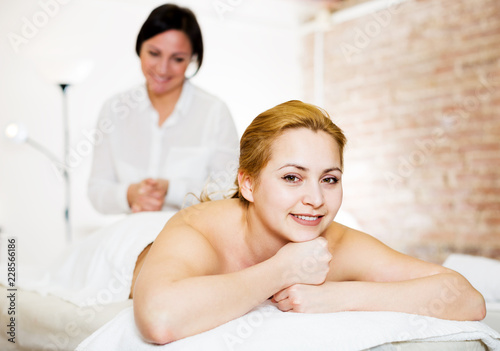 Masseuse massaging back zone of young smiling  woman