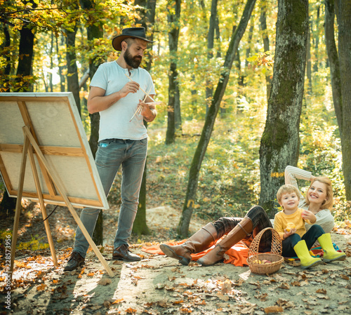 Autumn garden party - Father, mather and son. Camping with kids. Enjoying good weather. Man artist painting autumn picture.