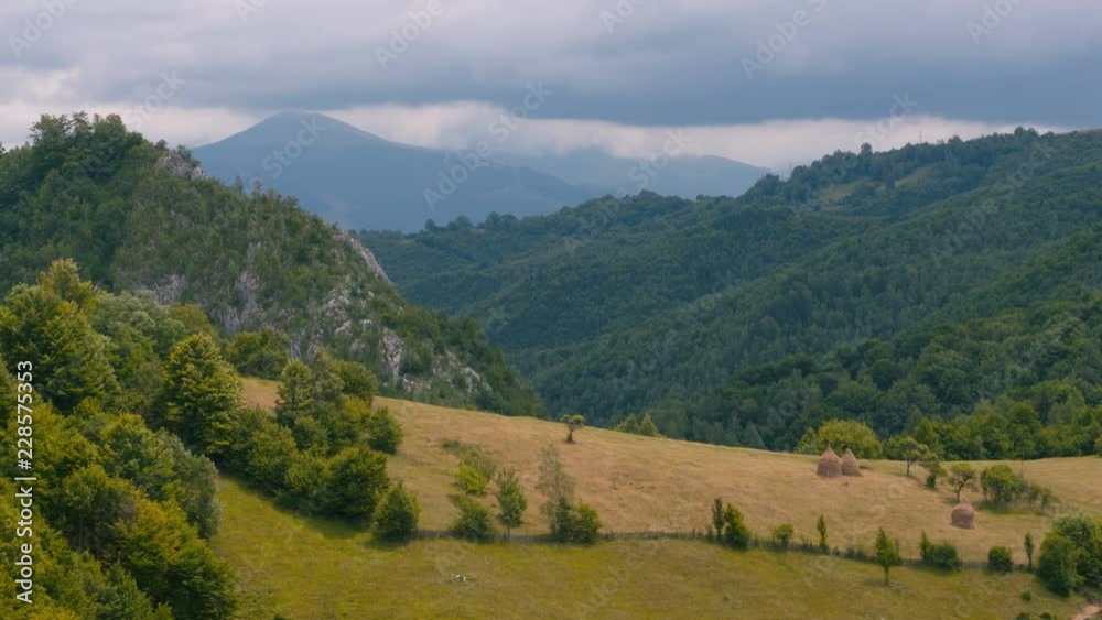 Romanian mountain landscape with meadow and haystacks. Wooded hills and mountain on background Romanian mountain landscape with meadow and haystacks. Wooded hills and mountain on background