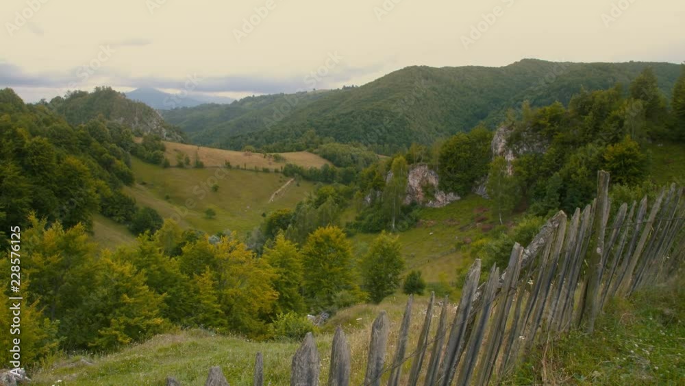 Romanian mountains landscape. Green valley, meadows, fence, wooded hills and mountain