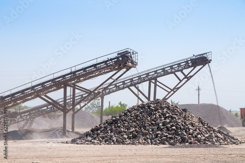 Crushing machinery, cone type rock crusher, conveying crushed granite gravel stone in a quarry open pit mining. Processing plant for crushed stone and gravel. Mining and Quarry mining equipment.