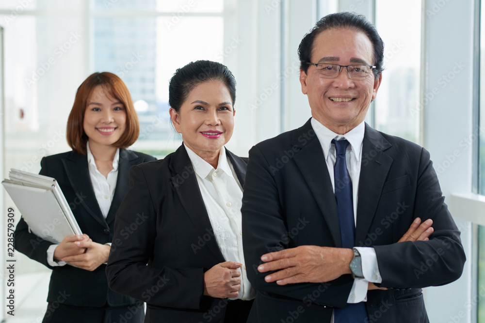 Portrait of successful Asian business team of three standing in modern office Portrait of successful Asian business team of three standing in modern office