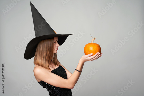 Profile portrait of Halloween witch holding orange pumpkin on palm looking at it, isolated on grey background photo