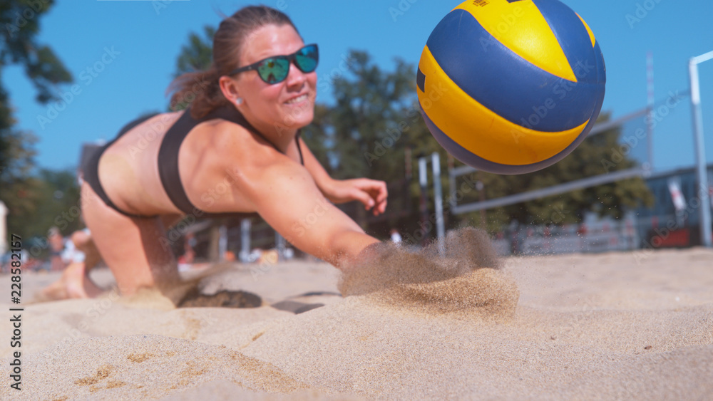 Obraz premium CLOSE UP: Young female volleyball player dives into the sand to save a point.