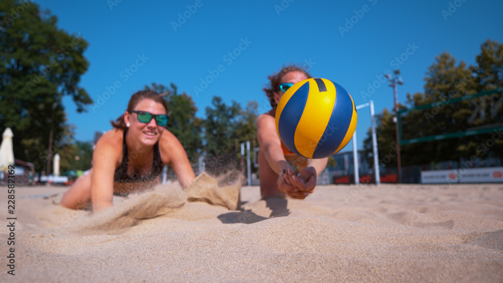 CLOSE UP: Female teammates both dive for ball during a beach volleyball game.