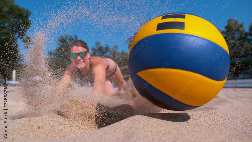 CLOSE UP: Athletic girl playing volleyball dives into the sand to reach the ball