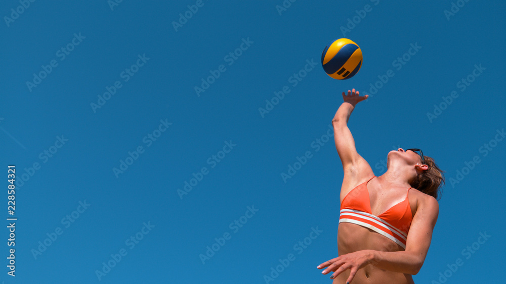 LOW ANGLE: Happy young woman in bikini serving ball during beach volleyball game