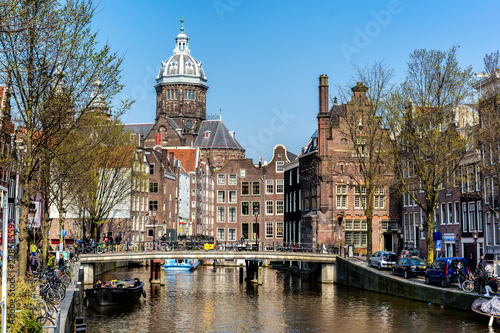 AMSTERDAM, NETHERLANDS - APRIL 11, 2018: St. Nicholas Church and Amsterdam canal with typical dutch houses. St. Nicholas Church is the city's primary Roman Catholic church.