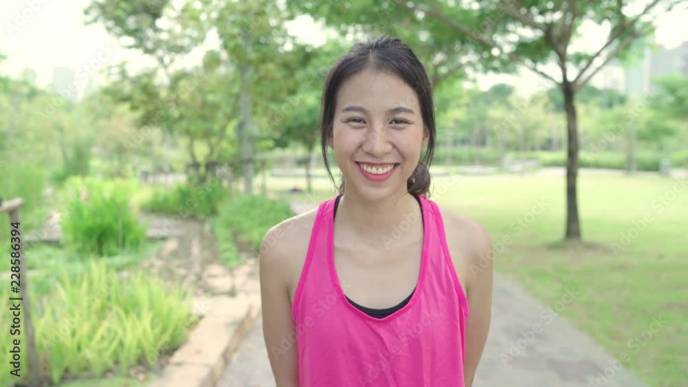 Healthy beautiful young Asian runner woman feeling happy smiling and looking to camera after running on street in urban city park. Lifestyle fit and active women exercise in the city park concept. Healthy beautiful young Asian runner woman feeling happy smiling and looking to camera after running on street in urban city park. Lifestyle fit and active women exercise in the city park concept.