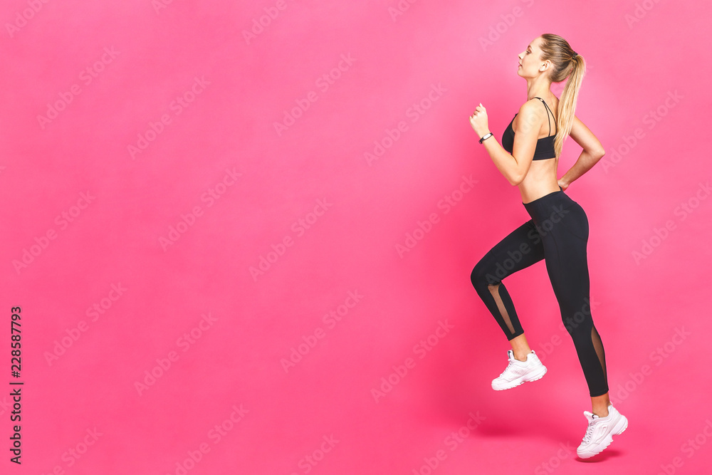Young beautiful woman with fit body jumping and running isolated over pink background. Female model in sportswear exercising.