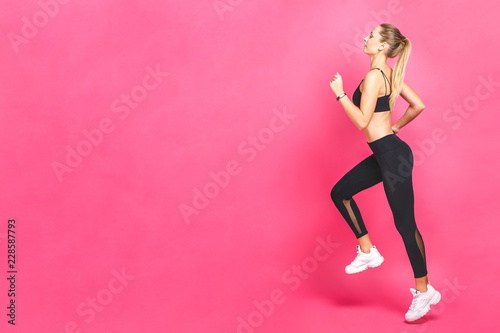 Young beautiful woman with fit body jumping and running isolated over pink background. Female model in sportswear exercising.