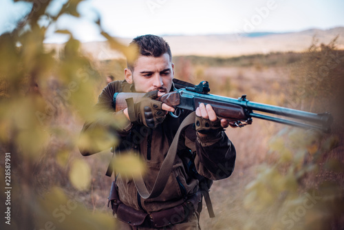 Hunter aiming rifle in forest. Hunter with shotgun gun on hunt. Track down.