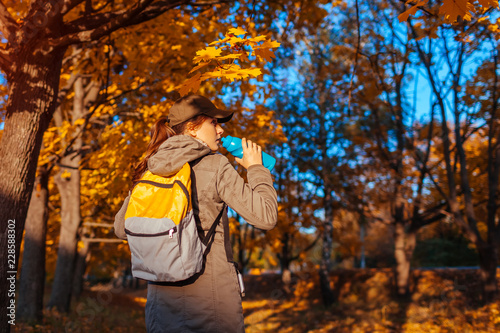 Tourist with backpack walking in autumn forest. Young woman drinking water