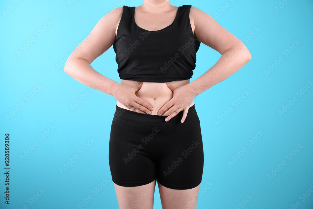 Overweight woman touching belly fat before weight loss on color background Overweight woman touching belly fat before weight loss on color background