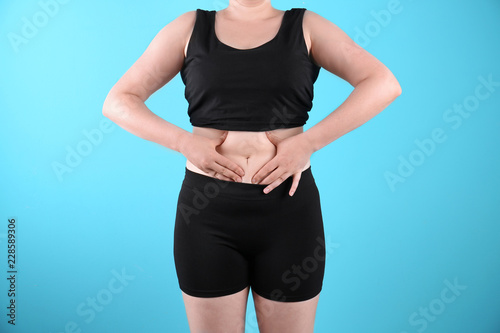 Overweight woman touching belly fat before weight loss on color background