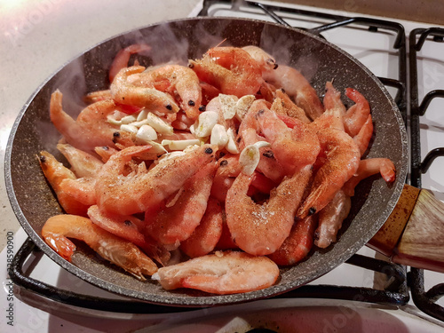Giant orange shrimps with heads fried in oil in a frying pan on a gas stove 