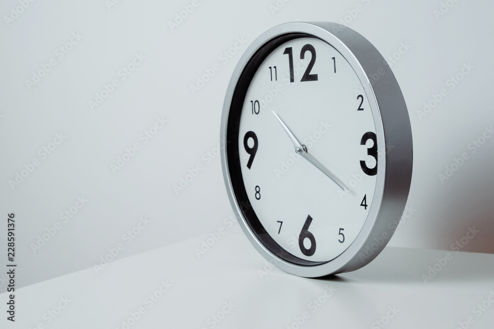 A view of a silver, large wall clock. Side view of a clock showing the time lying on a white