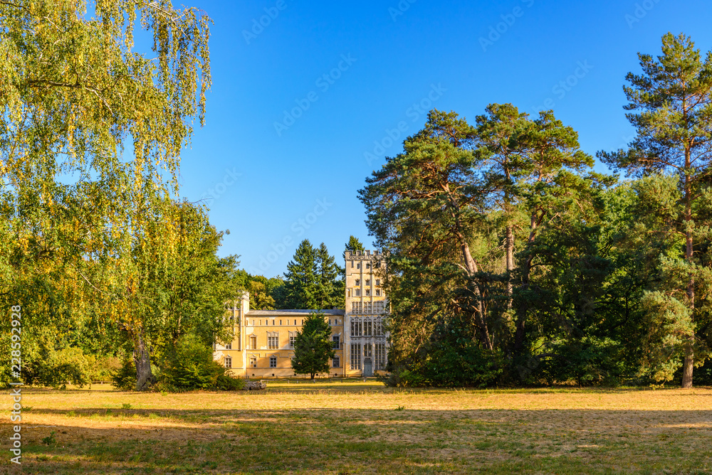 Fototapeta premium Sceneria domu, Kavaliershaus, otoczonego drzewami na Pfaueninsel, Peacock island, położonego nad jeziorem Wannsee w Berlinie w Niemczech w sezonie jesiennym i przy zachodzie słońca.