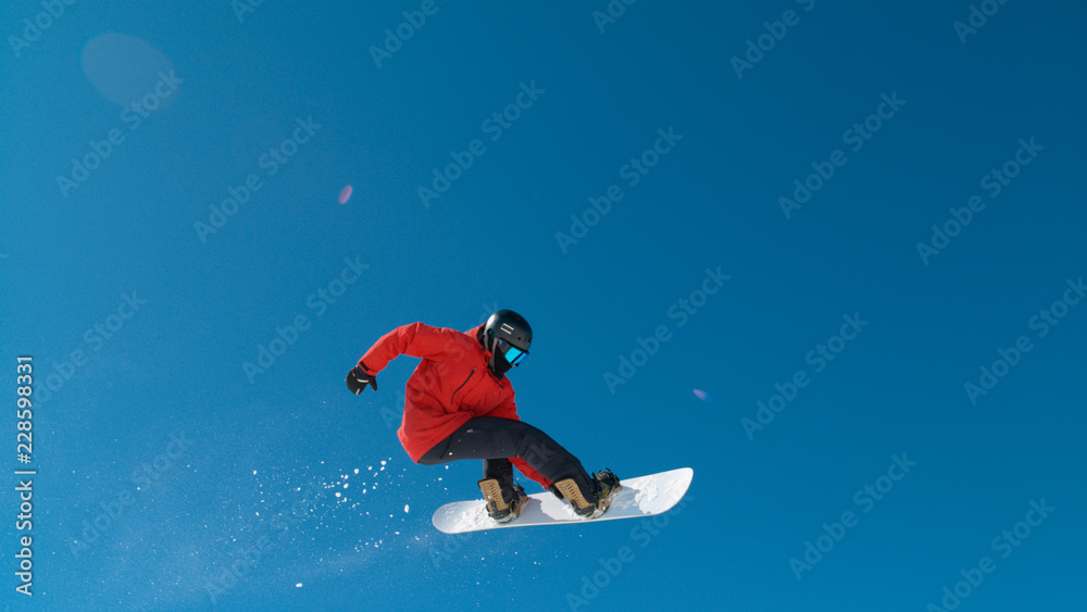 Awesome male snowboarder riding on a sunny day doing a trick high up in the air.