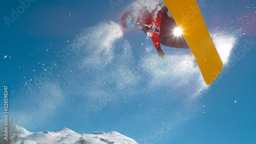 CLOSE UP: Athletic young male snowboarding spins in the air while doing a grab.