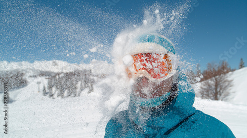 CLOSE UP: Smiling girl wearing ski goggles gets hit in the head by a snowball. © helivideo
