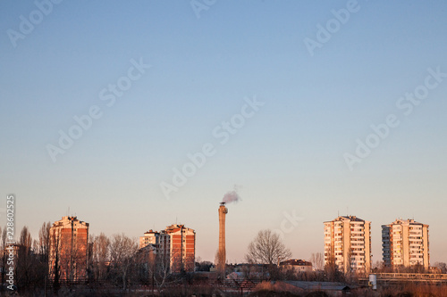 Communist housing buildings facing a polluting chimney smoking & an abandoned factory in Pancevo, Serbia. The towers are a symbol of Socialist architecture and  economic transition of Eastern Europe photo