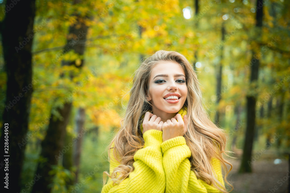Beautiful young happy girl with bright red-yellow leaf in park. Beautiful fashion woman in autumn red dress with falling leaves over nature background. Dreamy girl with long hair in knit sweater.