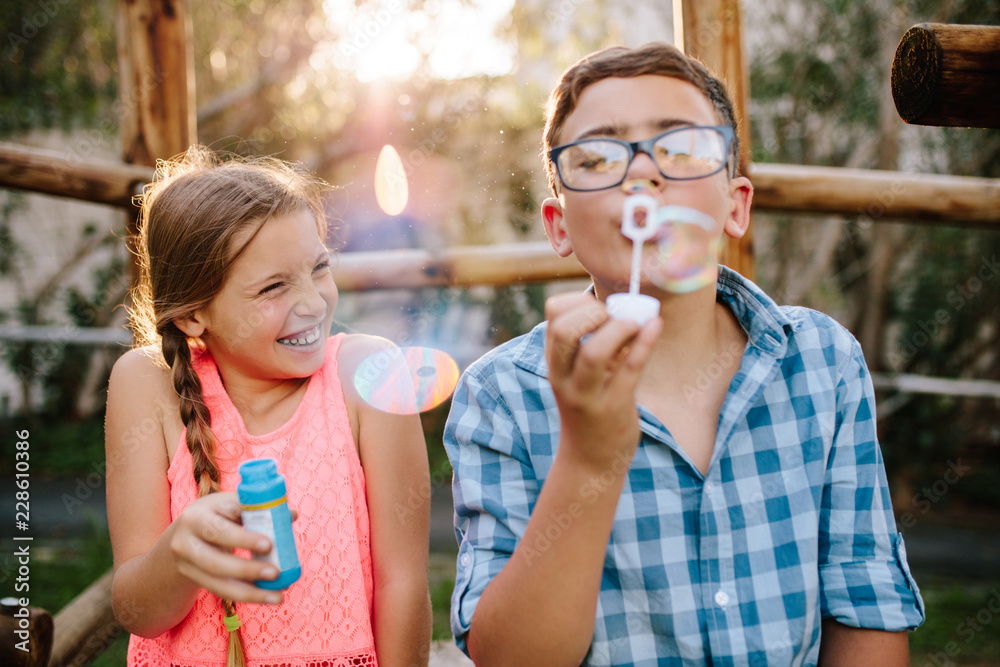 Fototapeta premium Young boy and girl having fun blowing soap bubbles