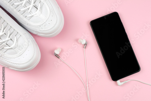 Equipment for running. Sport shoes. Sneakers and mobile phone with headphones. pink background. active lifestyle, fashion concept.