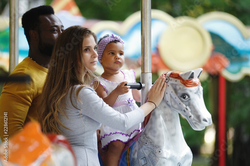 African American father and a white mother with a daughter in her arms. Family on the carousel.