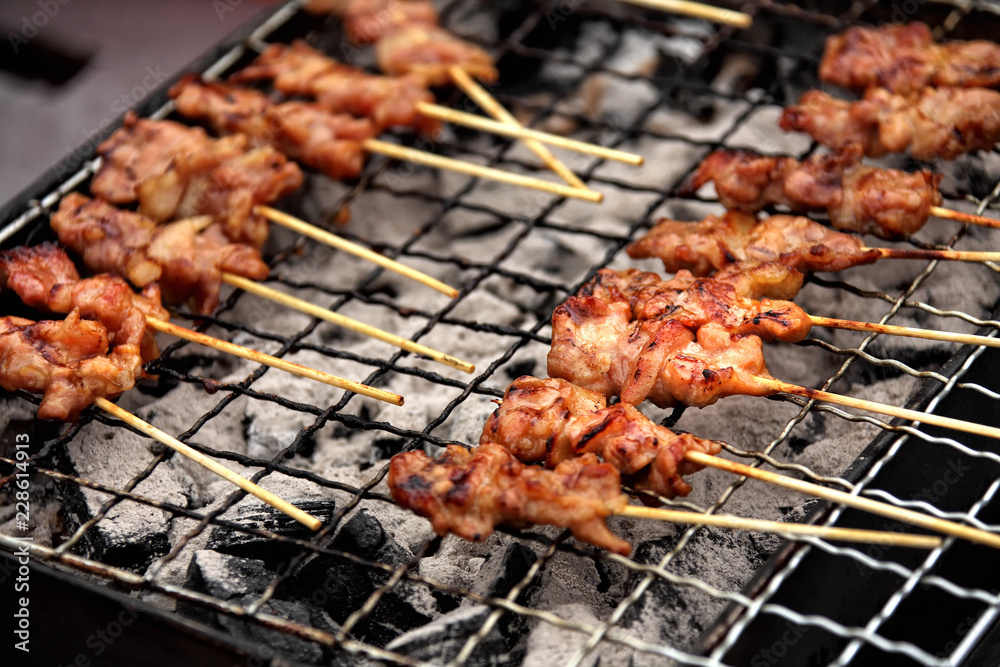 close up shot of grilling chicken meat on wooden stick in street market of Bangkok, Thailand