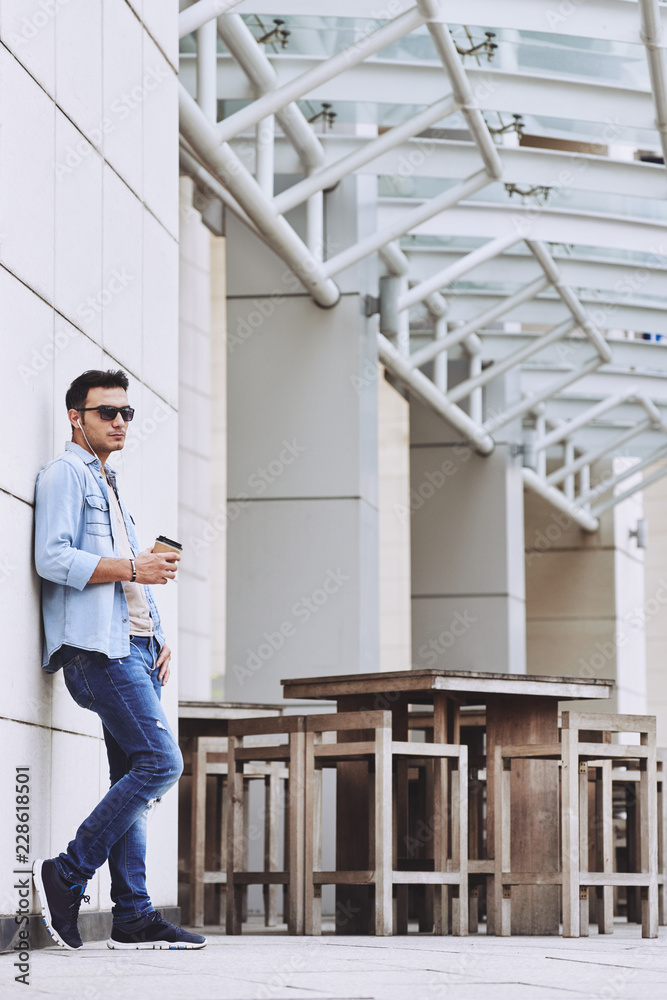 Stylish young man in sunglasses standing outdoor with cup of coffee Stylish young man in sunglasses standing outdoor with cup of coffee