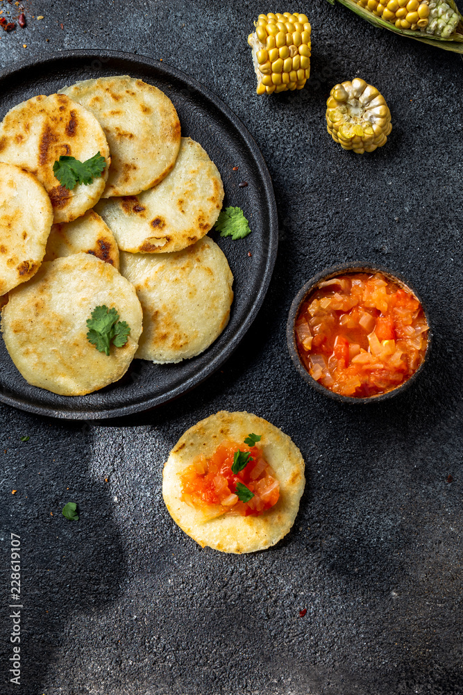 COLOMBIAN FOOD. Maize AREPAS and fried pork chicharron ans colombian tomato sauce. Top view. Black background COLOMBIAN FOOD. Maize AREPAS and fried pork chicharron ans colombian tomato sauce. Top view. Black background