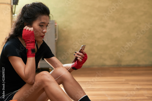 Young sporty woman restting on gym floor and checking text messages in phone © DragonImages