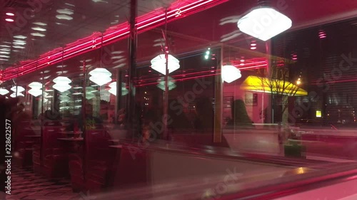 Diner reflection that's out of focus and blurred shows waitress taking order from table with other customers and tables in background. 