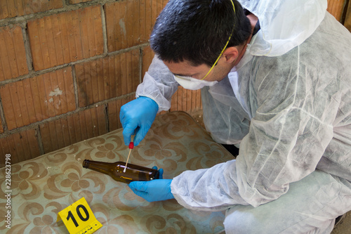 A forensic expert at the crime scene. He takes a DNA sample with a stick on the bottle photo