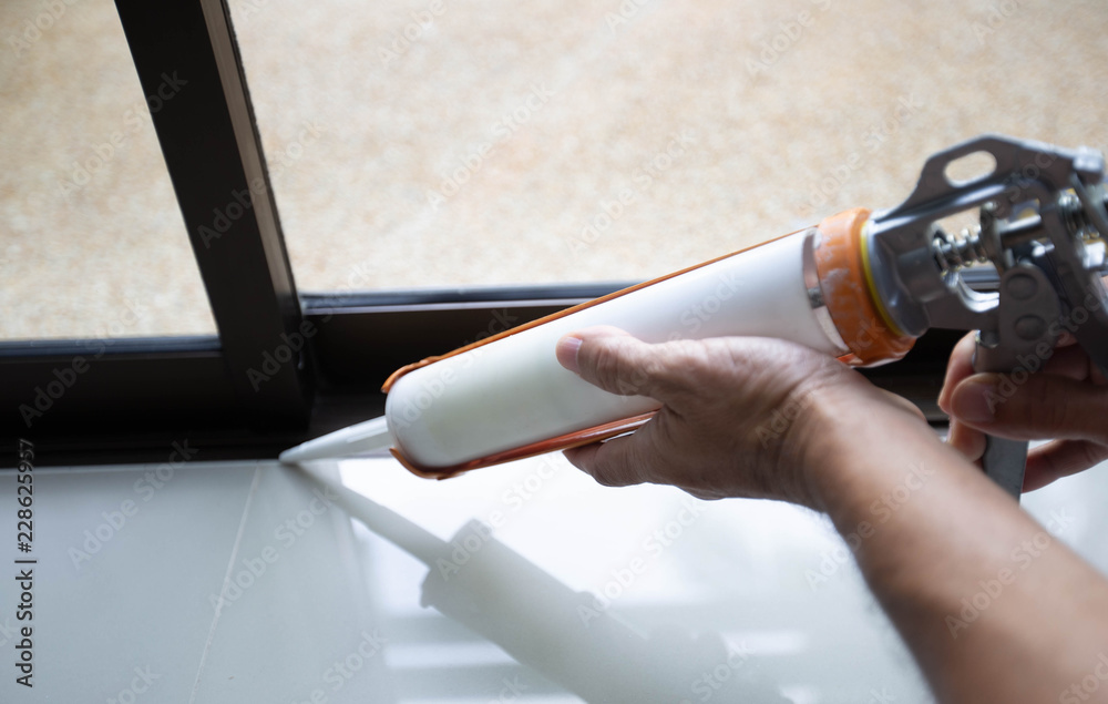 Men's hand uses silicone adhesive with a glue gun to repair worn windows. - obrazy, fototapety, plakaty 