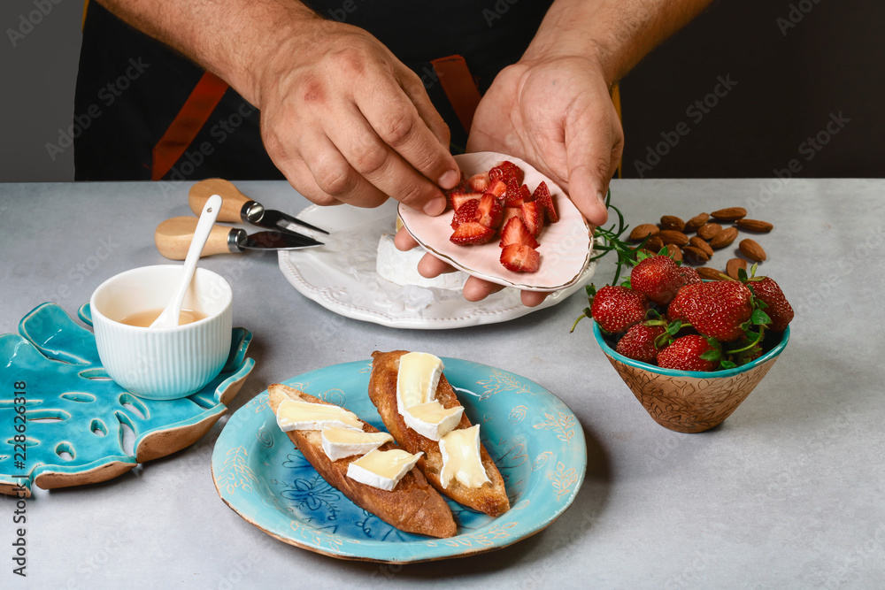 bruschetta cooking by chef hand. Sweet sandwiches with strawberries, cheese, camembert, brie, nuts and honey on light background