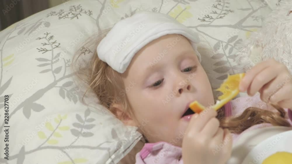 Sick girl with fever. A child with fever lies in bed and eats fruit. Sick girl with fever. A child with fever lies in bed and eats fruit.