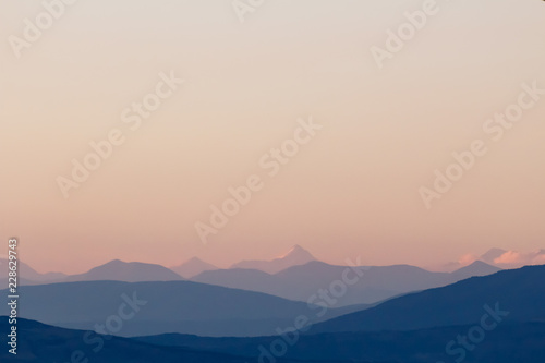 Purple mountain silhouettes and clear sky. Gradient from dark to light purple. Caucasus mountains.