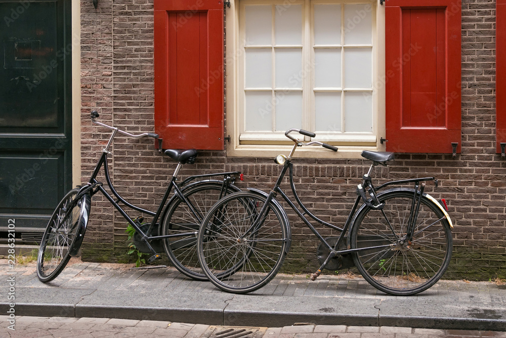 Two old black bicycles near red brick wall in the center of Amsterdam, Netherlands.