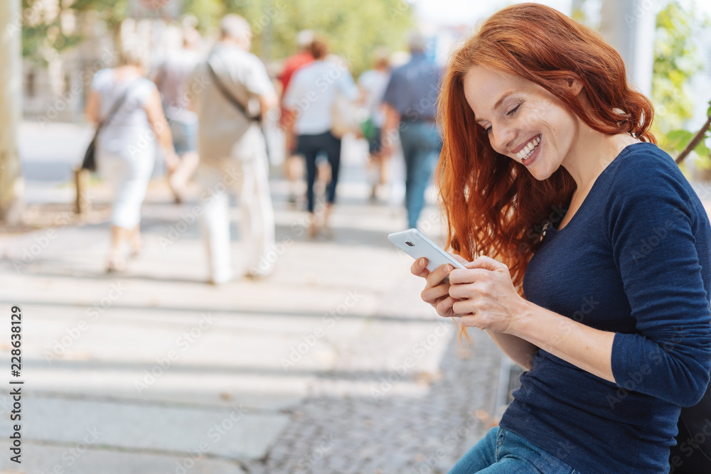 Smiling red haired woman using mobile in city