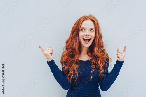 Excited young redhead woman pointing upwards photo
