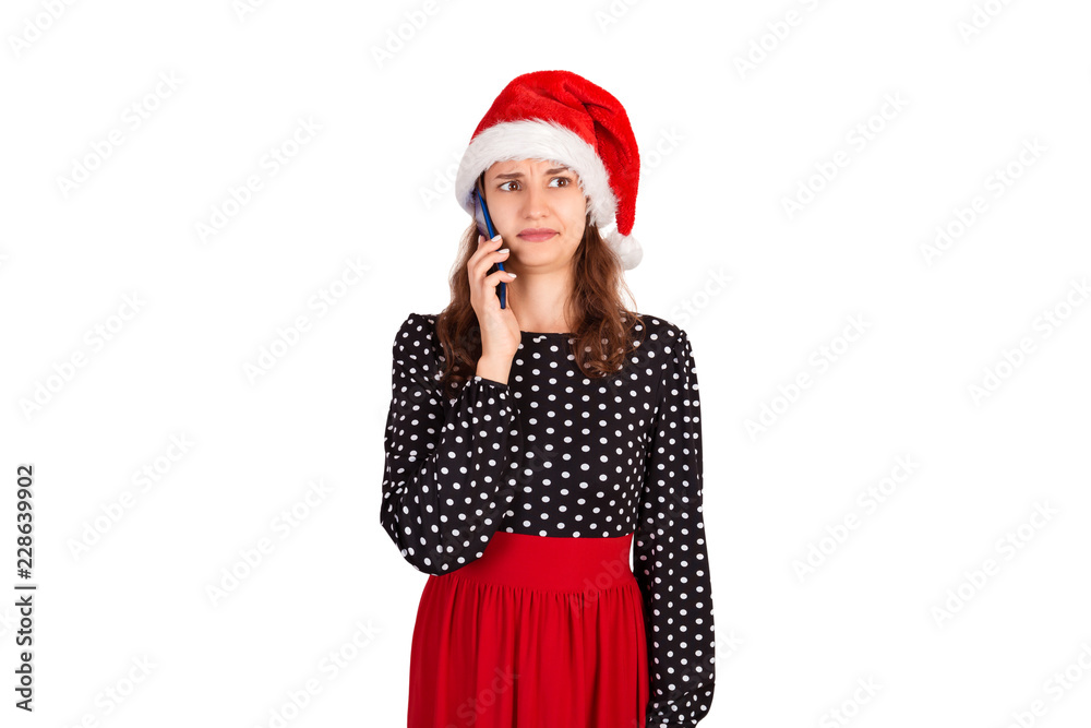 Portrait of confused young lady in dress talking on her phone. emotional girl in santa claus christmas hat isolated on white background. holiday concept Portrait of confused young lady in dress talking on her phone. emotional girl in santa claus christmas hat isolated on white background. holiday concept