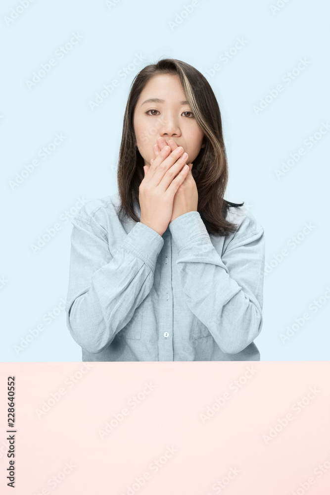 Young woman sitting at table covering her mouth isolated on blue. I can not say anything Young woman sitting at table covering her mouth isolated on blue. I can not say anything