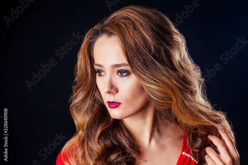 Portrait of young beautiful woman perfect skin, red lipstick with long brown hair in sexy red dress at studio on dark black background. beauty fashion model head shot