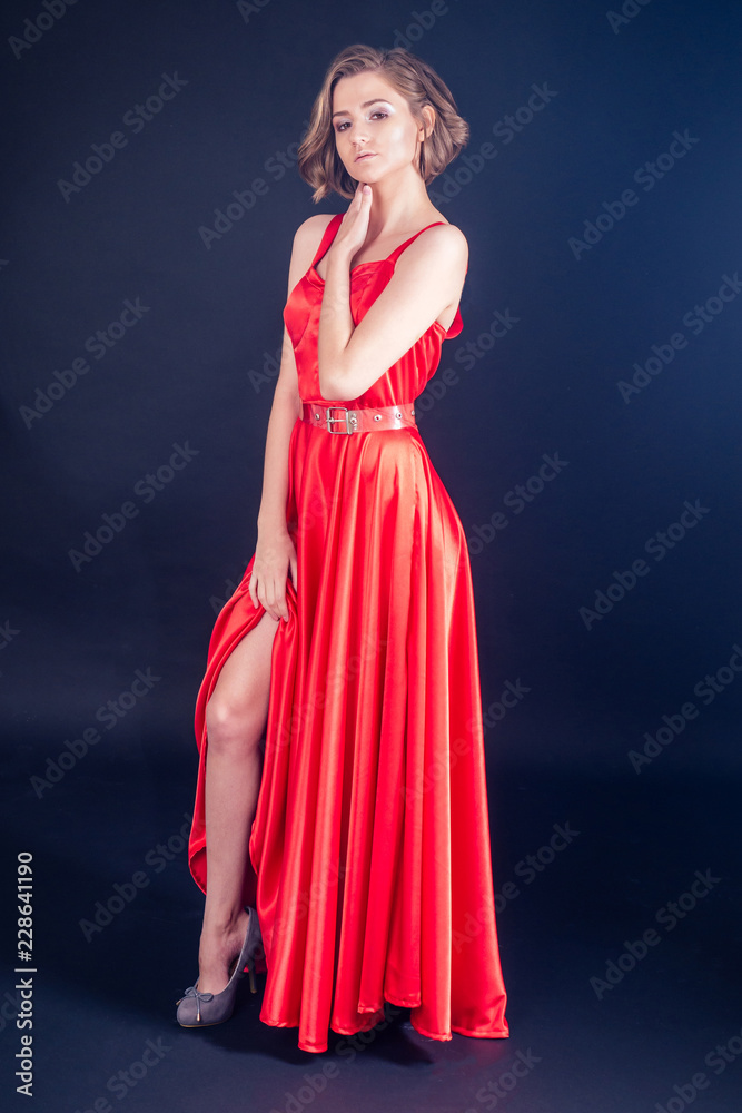 Portrait of young beautiful woman perfect skin, red lipstick with brown hair in sexy stylish silk red dress at studio on dark black background. beauty fashion photo model head shot wind in hair Portrait of young beautiful woman perfect skin, red lipstick with brown hair in sexy stylish silk red dress at studio on dark black background. beauty fashion photo model head shot wind in hair