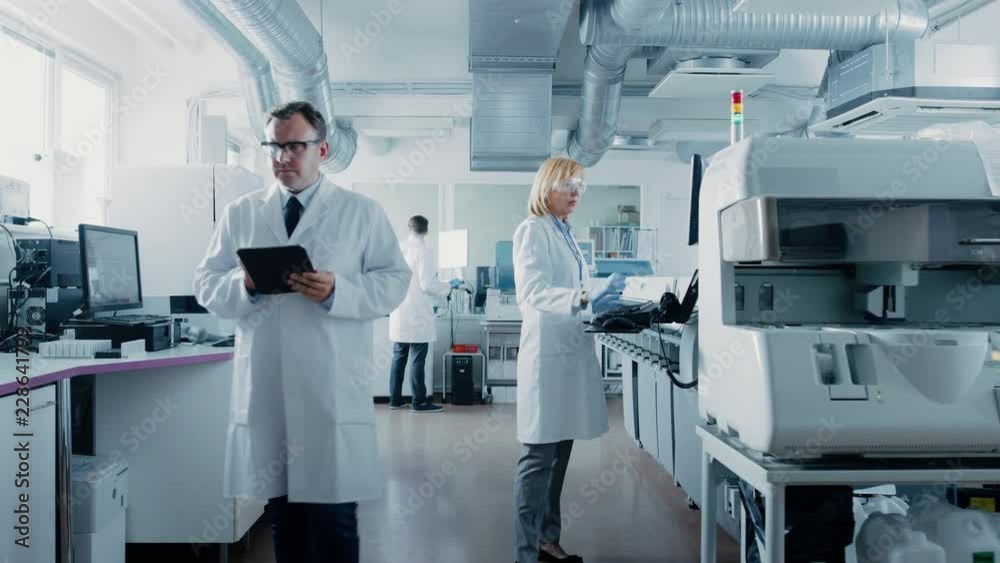 Team of Research Scientists Working On Computer, with Medical Equipment, Analyzing Blood and Genetic Material Samples with Special Machines in the Modern Laboratory.
