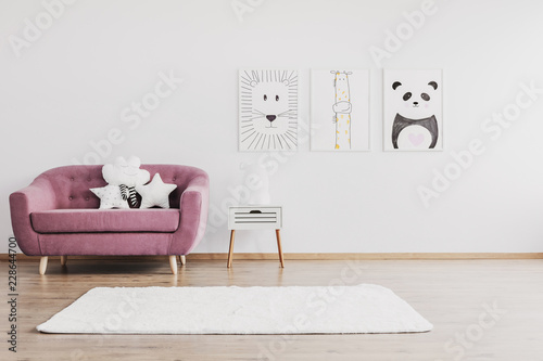 Stylish pink couch with cute pillows in spacious baby room interior with animals posters on the wall